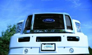 Close-up of a white Ford F-Series limo's front grill and bumper, featuring a "Tiffany Coach" license plate.