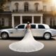 Bride in wedding gown standing by a white limousine outside a mansion. Wedding planning.