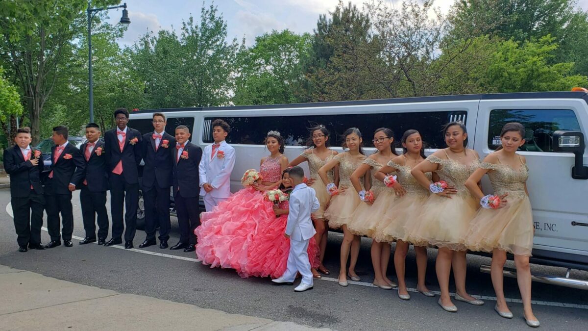 Group of teens in formal wear posing by a white party bus for a Quinceañera.