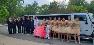 Group of teens in formal wear posing by a white party bus for a Quinceañera.