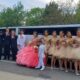 Group of teens in formal wear posing by a white party bus for a Quinceañera.
