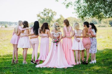 Bride and bridesmaids in pink dresses, posing outdoors for a bridal shower.