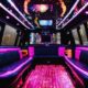 Luxurious party bus interior with pink and black leather seating, colorful LED lighting, and a flat-screen TV. Perfect for NJ nightlife!